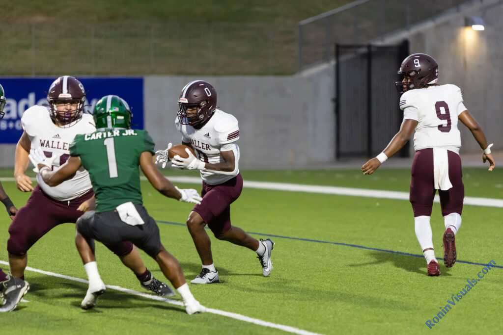 Leighton Geiman (58, obscured) blocks for Alex Barrs (0) after the handoff from quarterback Jordan Duncan (9) from the Bulldogs' own endzone. The Waller Bulldogs break their losing streak with a victory over Katy Mayde Creek’s Rams, 35-0, at Legacy Stadium, Saturday, Sept. 2, 2023. (Photo courtesy RoninVisuals.com)